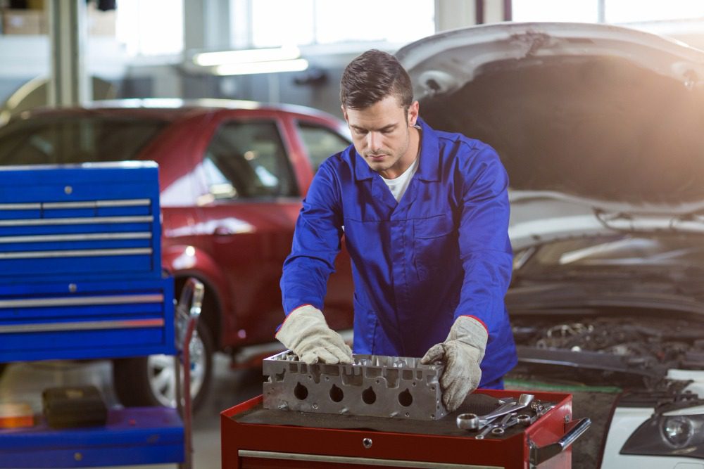 Auto mechanic in blue uniform working on car engine part in garage