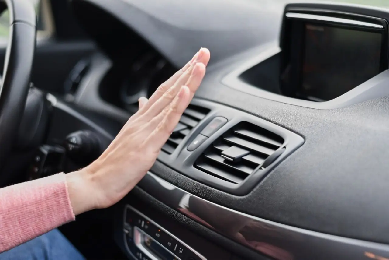 Person checking airflow from car air conditioning vent by holding hand in front of dashboard vent.
