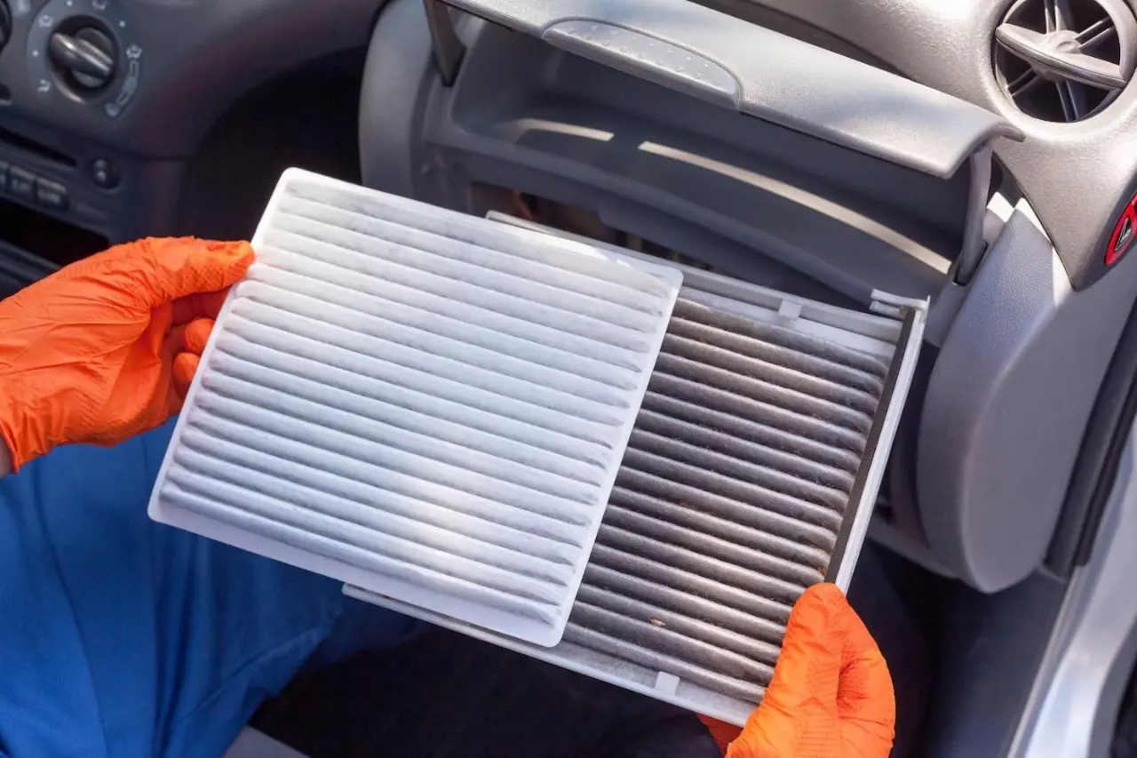 Mechanic compares clean and dirty cabin air filters side by side during replacement in car interior.