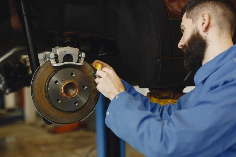 Mechanic in blue uniform inspecting and repairing a car disc brake rotor and caliper in workshop.