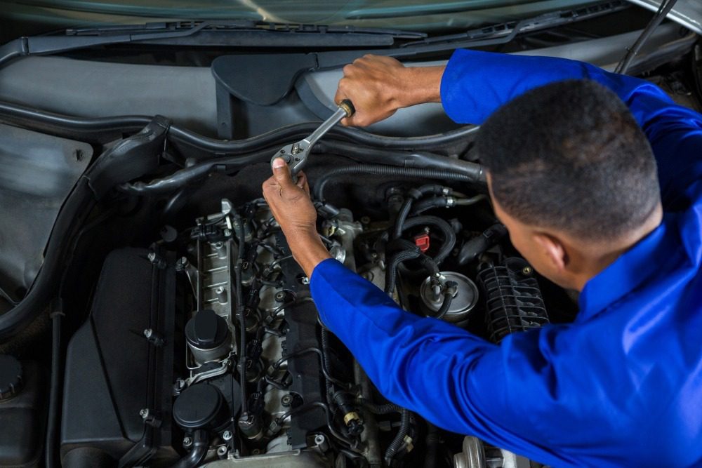 Mechanic tightening bolt in car engine bay with ratchet wrench