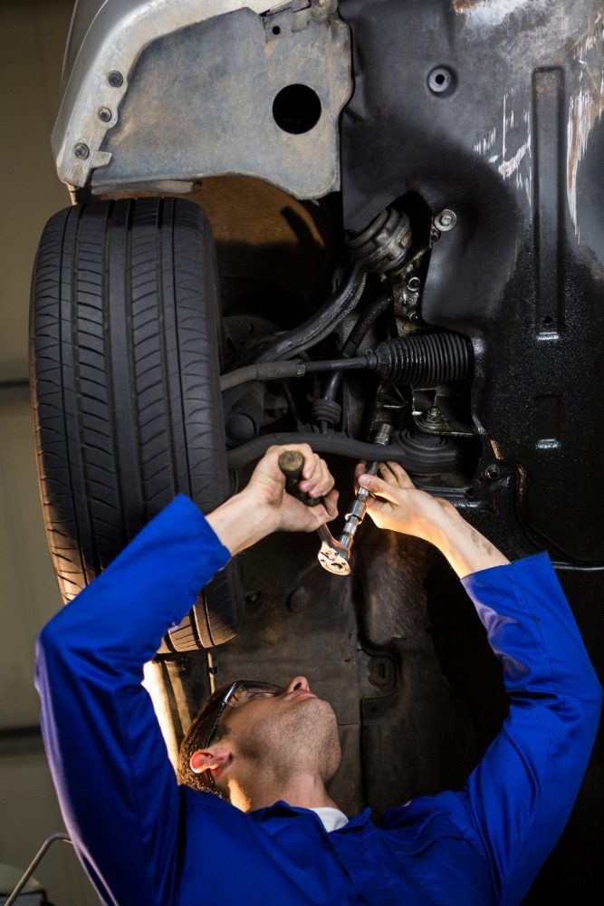 Mechanic using wrench on car undercarriage suspension in garage