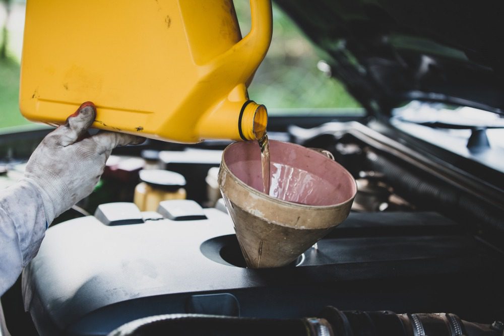 Mechanic pouring oil from yellow jug into funnel in car engine