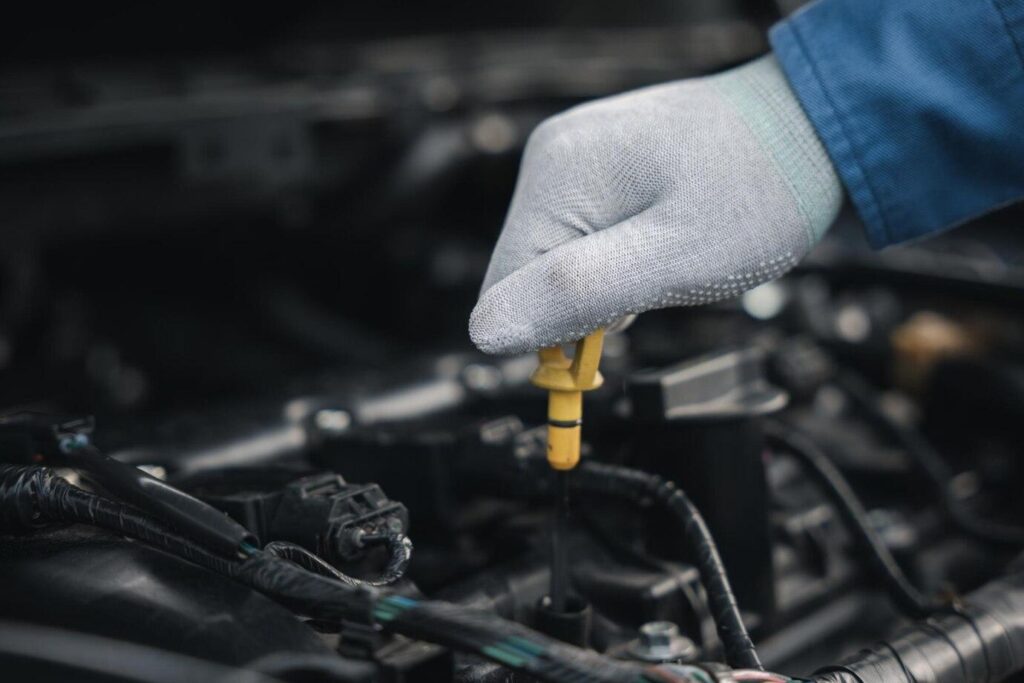 Mechanic hand in glove checking engine oil level with dipstick during routine car maintenance.