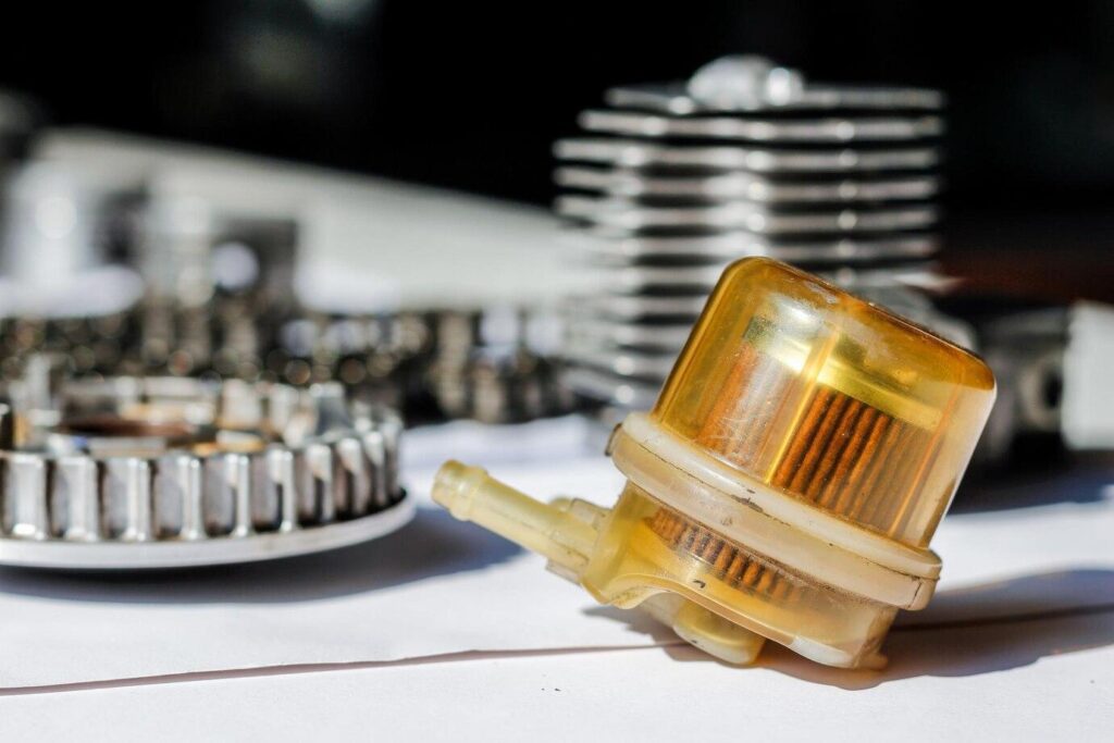 Close-up of a yellow fuel filter and metal engine components placed on a white surface in sunlight.