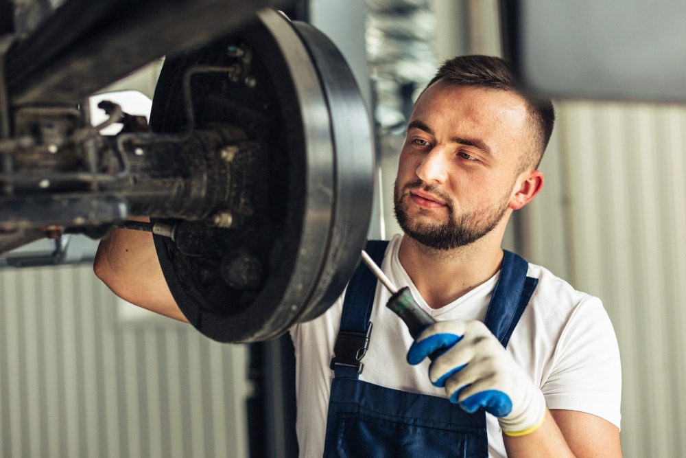 Mechanic in gloves and overalls inspecting and repairing a vehicle brake system with a screwdriver.