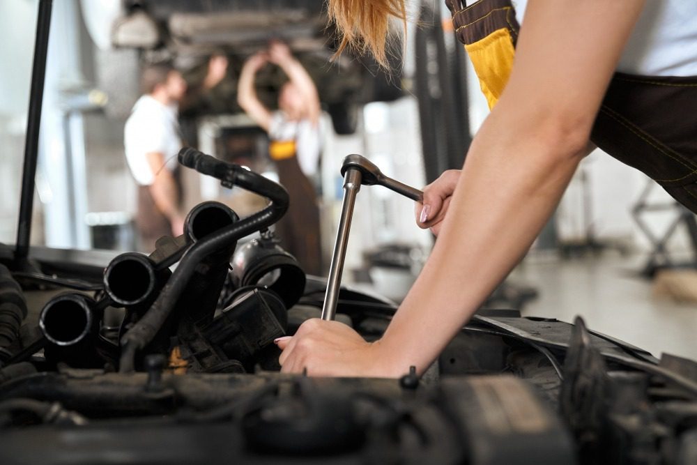 Mechanic using a wrench to repair a car engine in an auto repair shop.