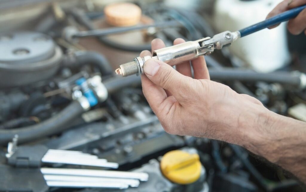 Mechanic’s hand holding spark plug with tool during car engine repair and maintenance service.